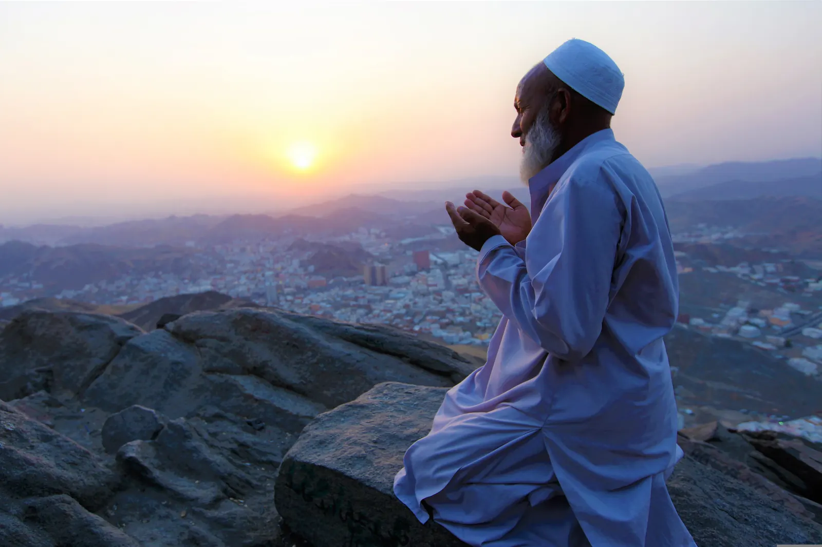 An elderly pilgrim raising his hands in supplication at sunrise