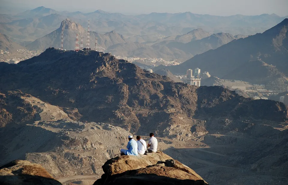Pilgrims in ihram sitting together on high ground above a mountain landscape